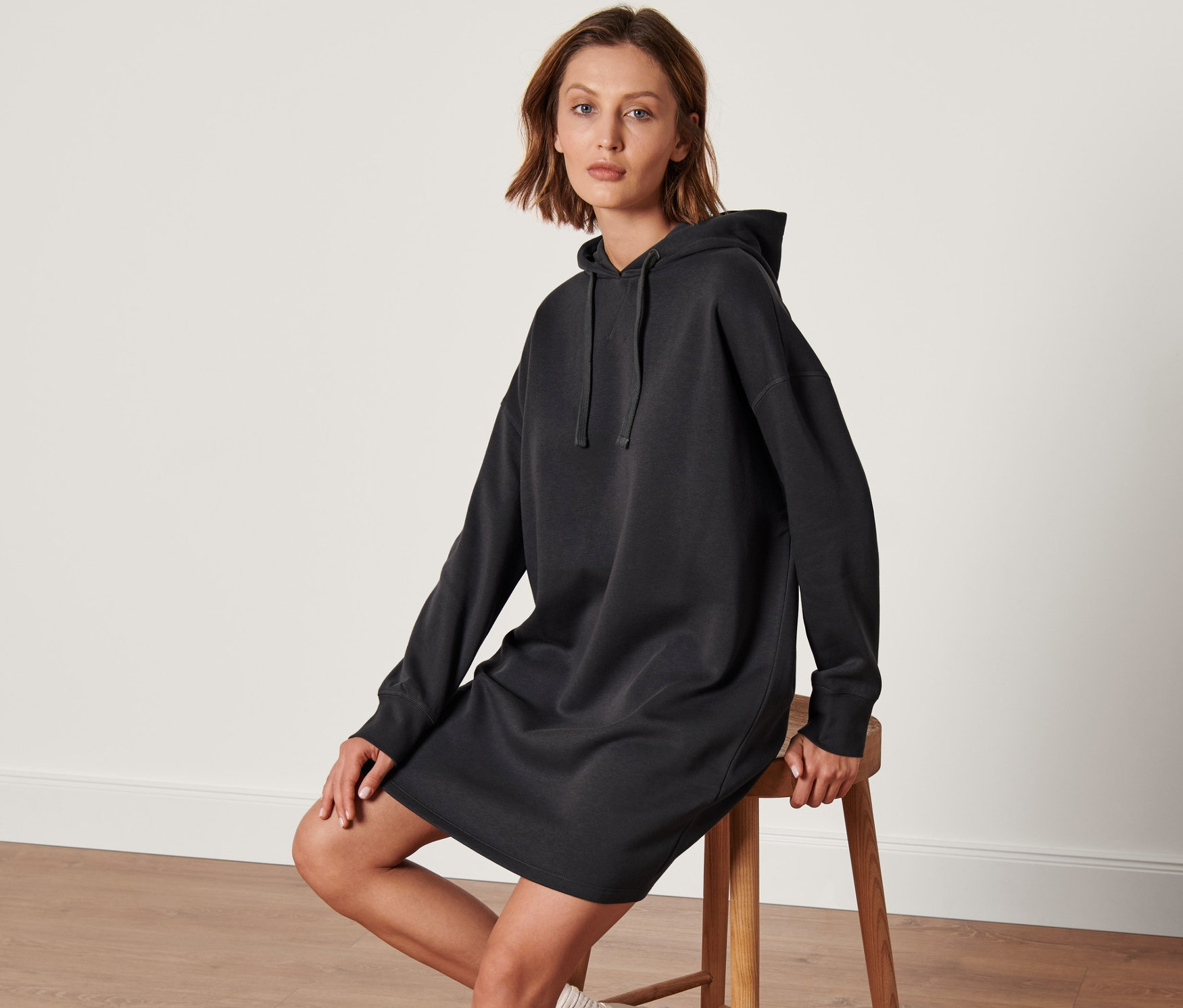 Frau sitzt auf einem Hocker und trägt ein Sweatkleid mit Kapuze.