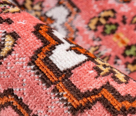Detailaufnahme eines gemusterten, roten Kurzflorteppichs.