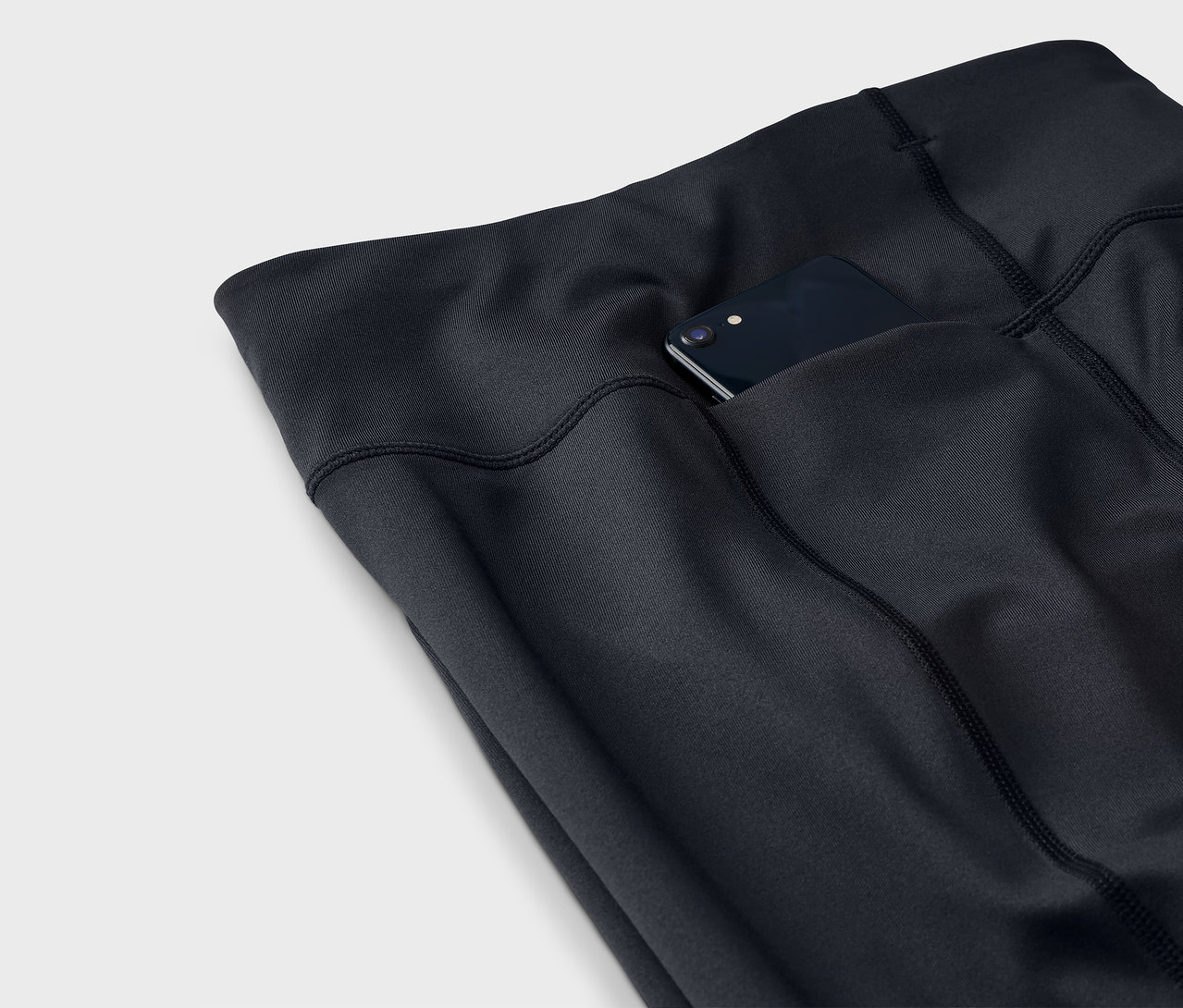 Detailaufnahme einer schwarzen Leggings mit einem Smartphone in der Tasche.