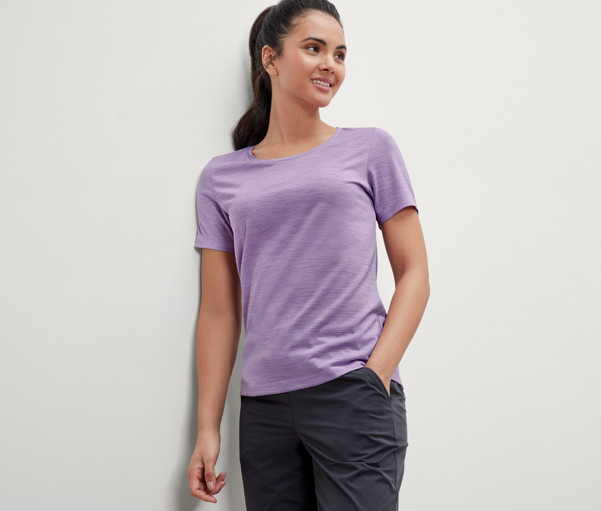 Frau, die sich an eine Wand lehnt, trägt ein lila T-Shirt mit Merinowolle.