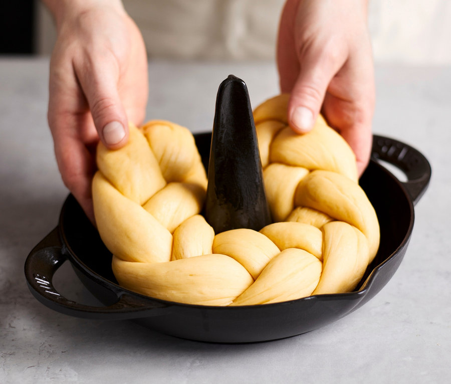 Eine Person legt einen geflochtenen Laib in einen schwarzen STAUB Hähnchen-Bräter.
