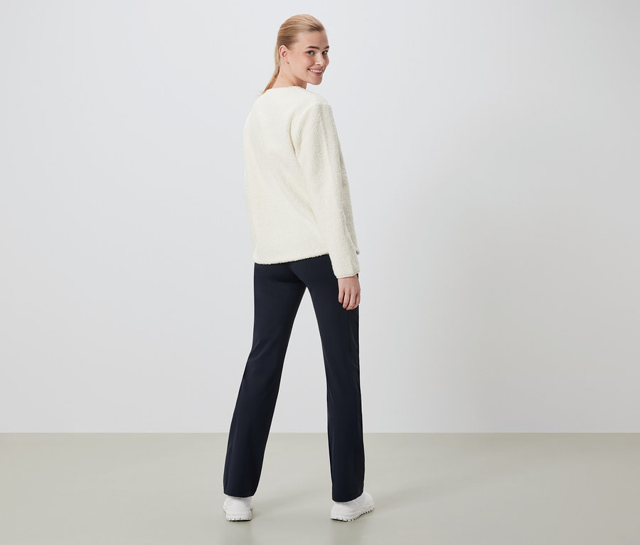 Frau blickt über die Schulter, trägt einen cremefarbenen Pullover und dunkelblaue Hosen.