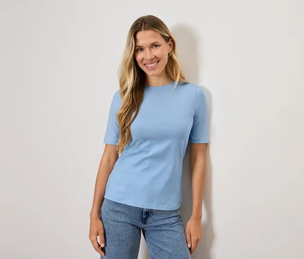 Frau mit blonden Haaren trägt ein hellblaues T-Shirt und Jeans.