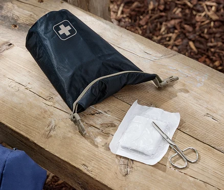 Eine geöffnete Erste-Hilfe-Tasche, eine Bandage und eine Schere liegen auf einer Holzbank.