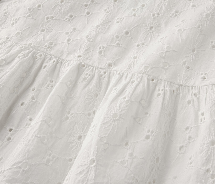 Detailansicht eines weißen Blusenkleids mit Lochstickerei.