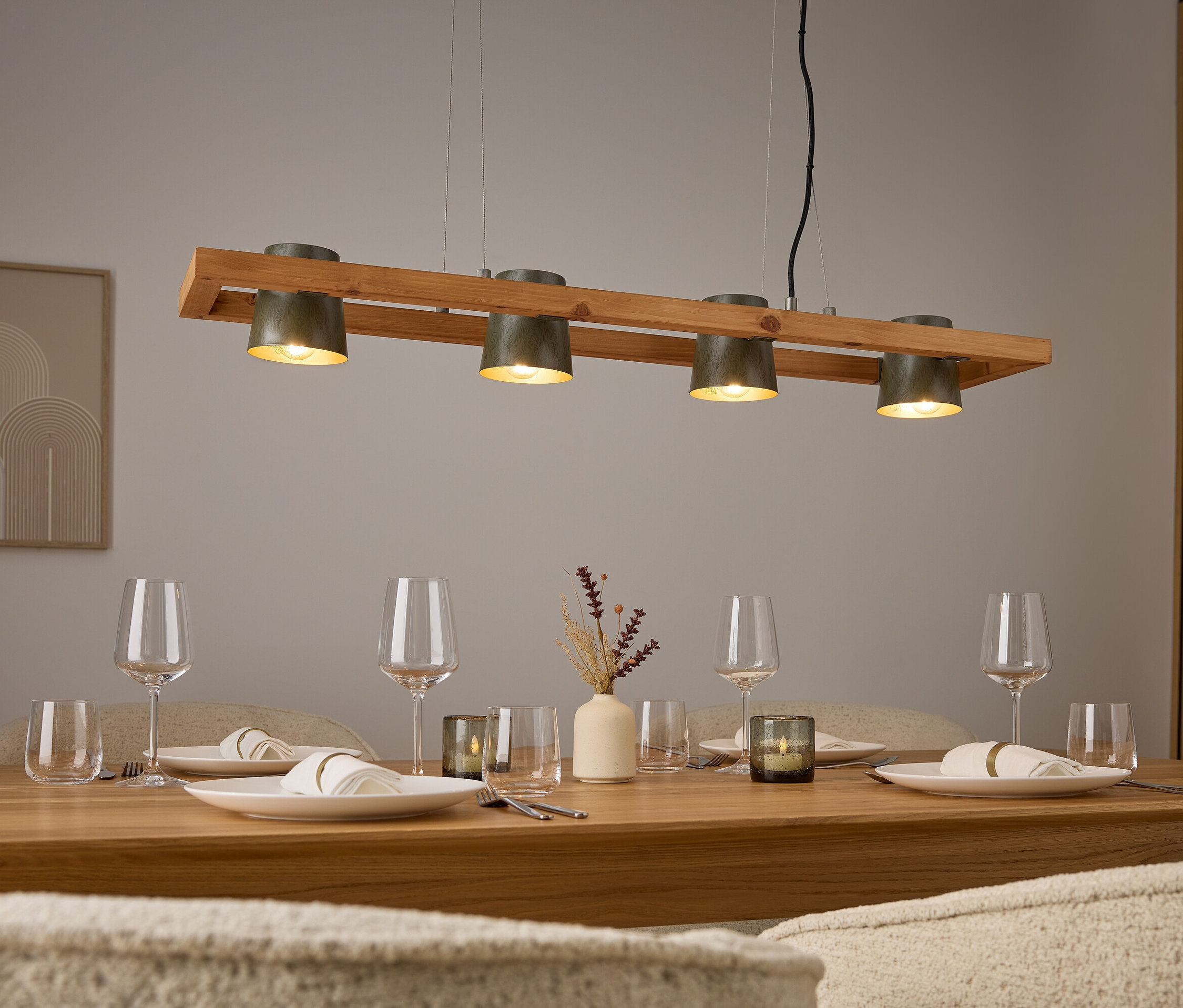 Vier graue Lampen über einem Holztisch mit Gedecken und Gläsern.
