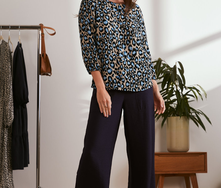 Frau trägt eine Bluse mit Print und dunkle Hosen.