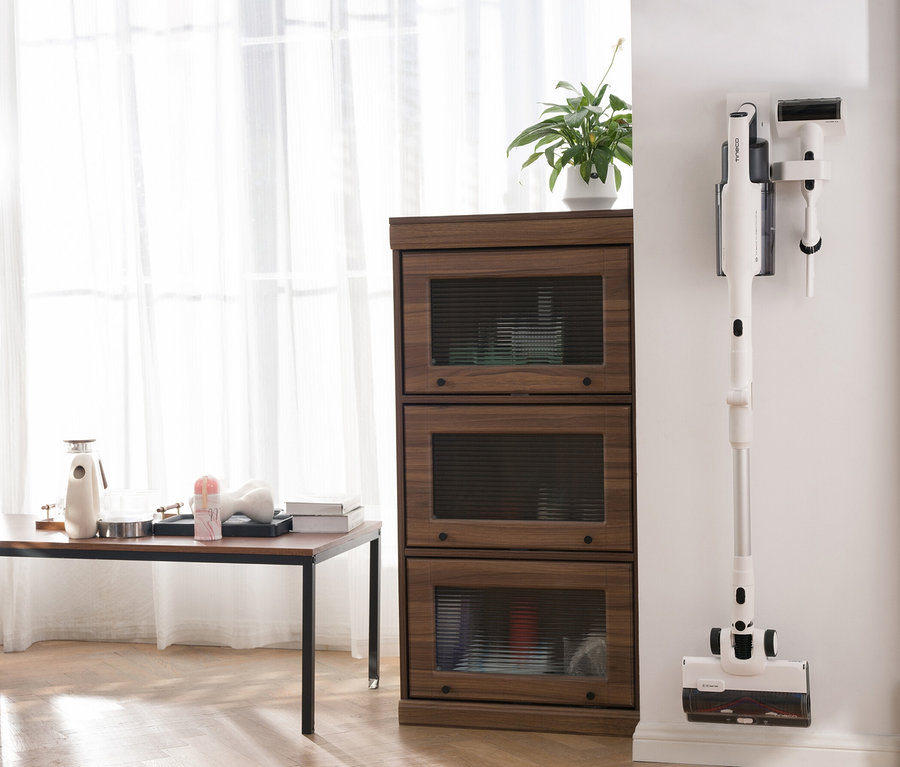 Ein Zimmer mit Fenster, Tisch und Schrank. An der Wand hängt ein Tineco Akku-Staubsauger »Pure One A50S«.