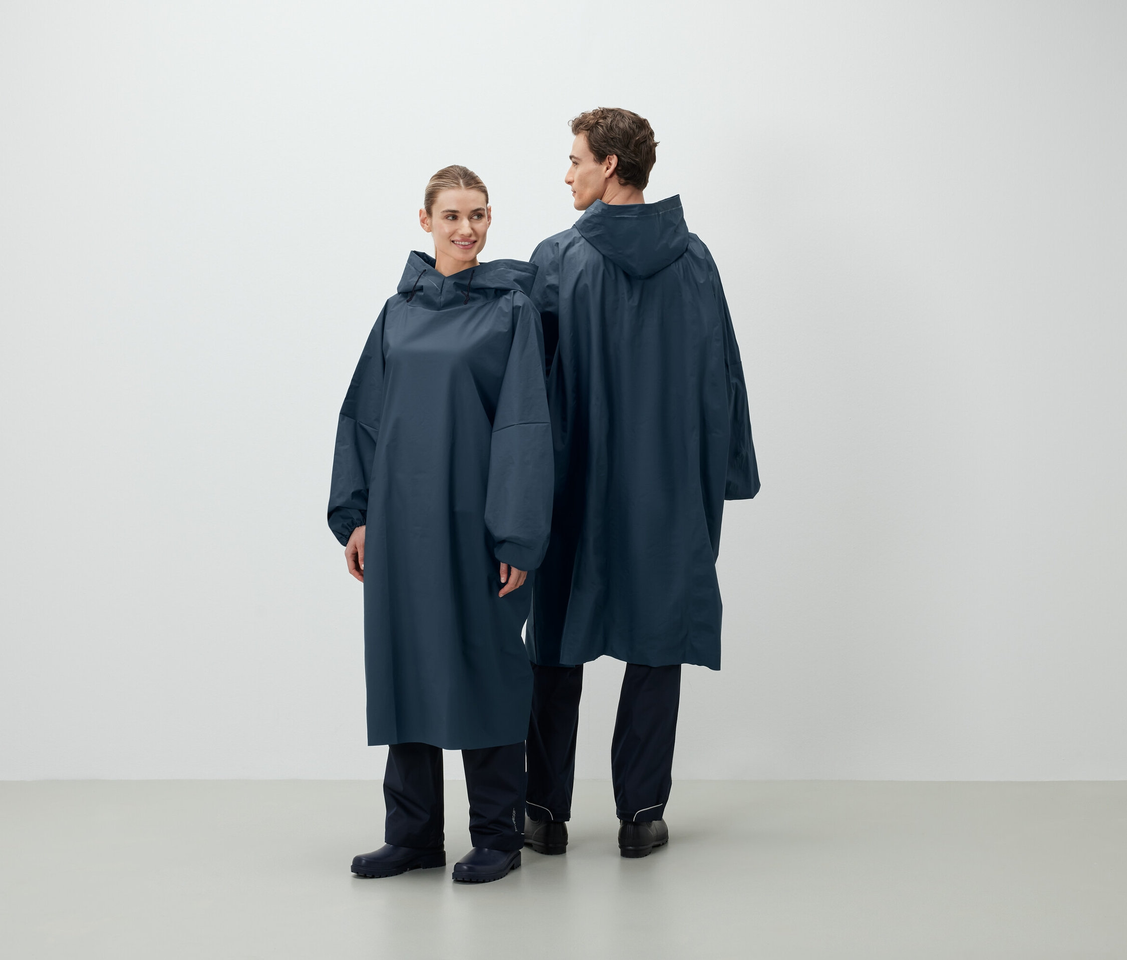 Zwei Personen posieren in langen, blauen Regenmänteln mit Kapuze.