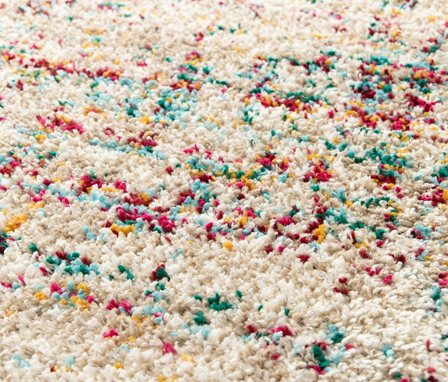 Detailansicht des beigen Zottelteppichs »Relic« mit gedämpften Pastellfarben.