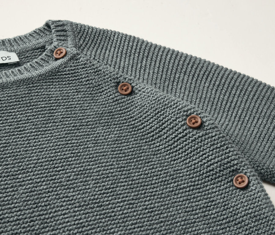 Detailaufnahme eines grauen Baby-Strickkombis mit braunen Knöpfen.