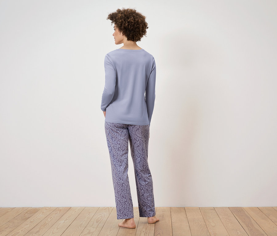 Frau mit dem Rücken zur Kamera trägt einen hellvioletten langen Pyjama und Hosen mit Blattdruck.