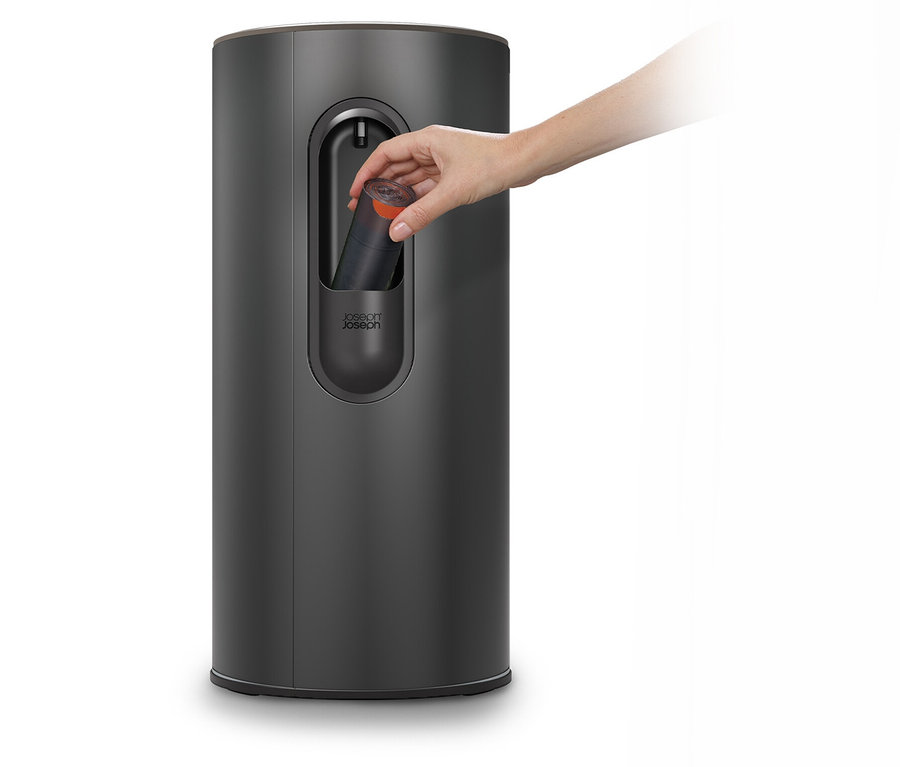 Eine Hand legt eine schwarze Flasche in einen grauen Spender.