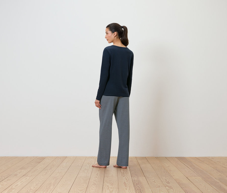 Eine Frau in einem dunkelblauen Pullover und gestreiften Hosen steht mit dem Rücken zur Kamera.