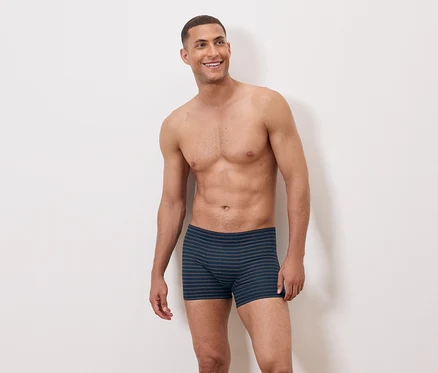Ein barober Mann trägt blaue gestreifte Boxershorts und lächelt.
