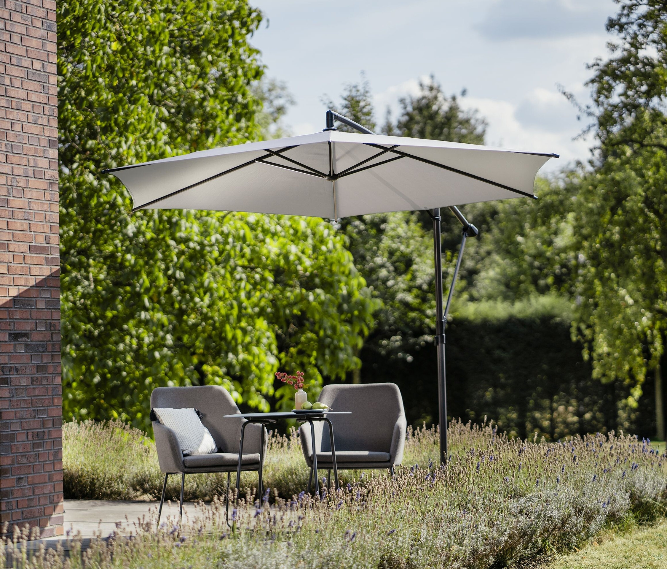 Zwei graue Sessel und ein Tisch stehen draußen unter einem hellgrauen Leco Ampelschirm Ø 300 cm, inkl. Schirmständer und Abdeckhaube.