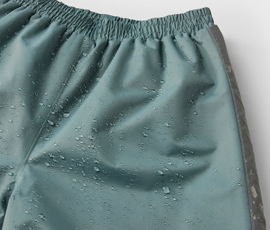 Detailaufnahme einer Kinder-Regenhose in Salbeigrün mit Wassertropfen.