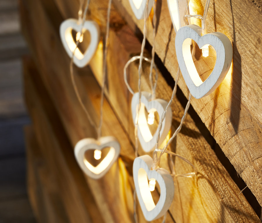 Nahaufnahme einer LED-Lichterkette mit hölzernen Herzformen vor einem Holzhintergrund.
