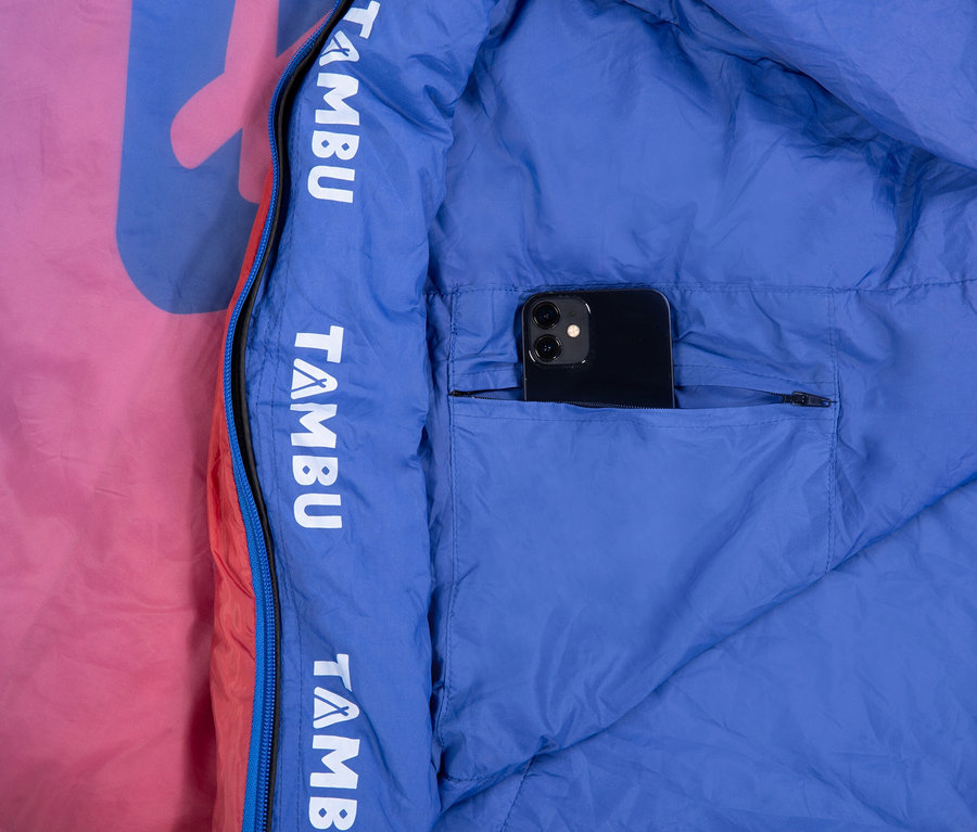 Handy in der Tasche eines geöffneten, blau gefütterten Schlafsacks mit Reißverschluss und pinkfarbener Außenseite.