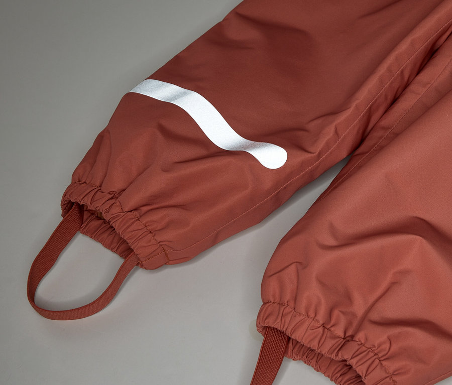 Nahaufnahme von zwei rostfarbenen Hosenbeinen mit elastischen Bündchen und weißen Reflektoren.