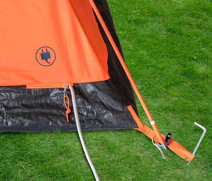 Detailaufnahme vom orangefarbenen Tambu »HAIKA 2« 2-Personen-Kuppelzelt auf einer Wiese, befestigt mit Heringen.