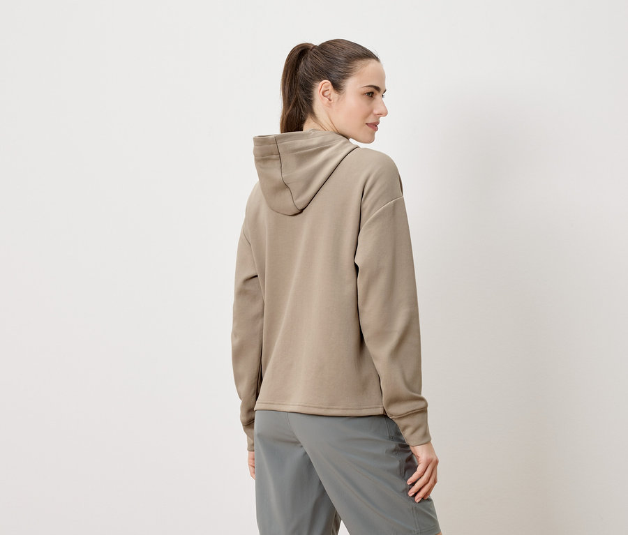 Frau von hinten, trägt einen beigen Kapuzenpullover und graue Shorts.
