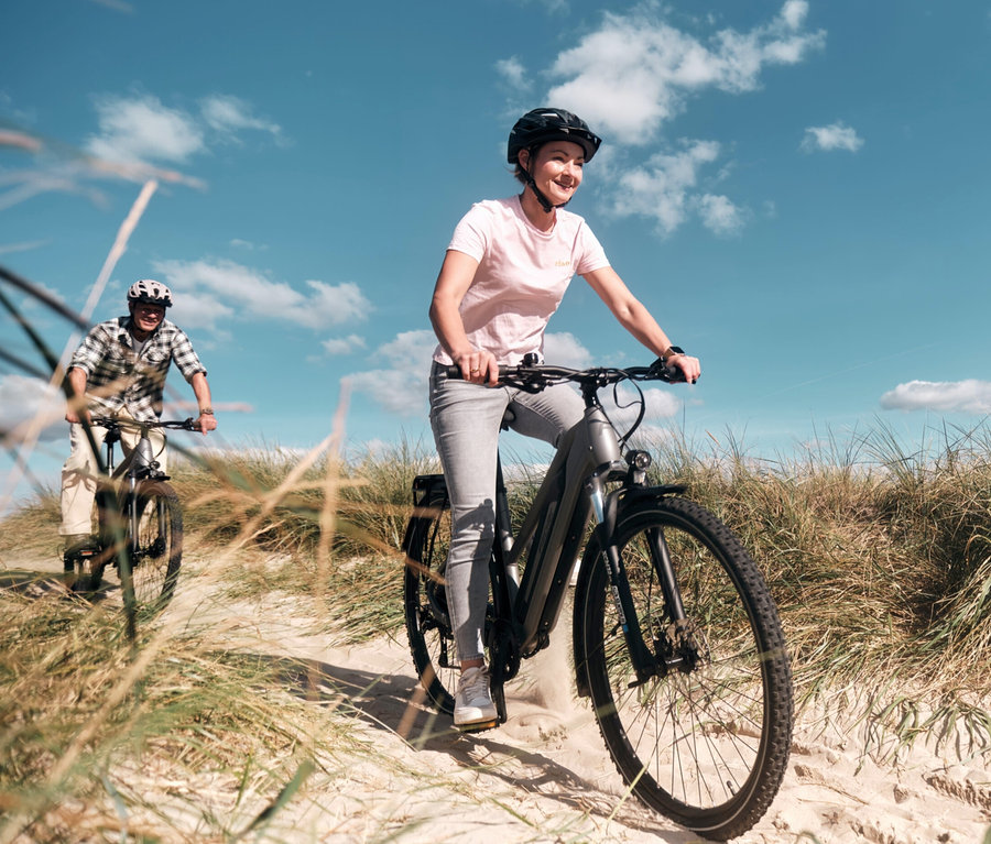 Frau fährt ein FISCHER Trekking-E-Bike TERRA 2.2 ACTIVE mit Trapez Rahmen. Ein Mann fährt auch ein E-Bike im Hintergrund.