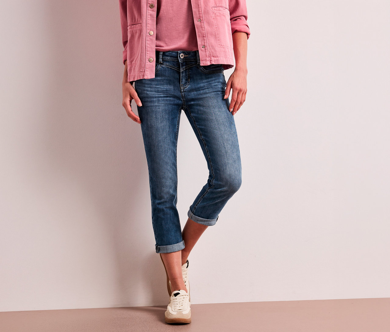 Eine Person trägt eine pinkfarbene Jacke, ein pinkfarbenes Oberteil, blaue, hochgekrempelte Street One 7/8-Jeans »Jane« und helle Sneaker.