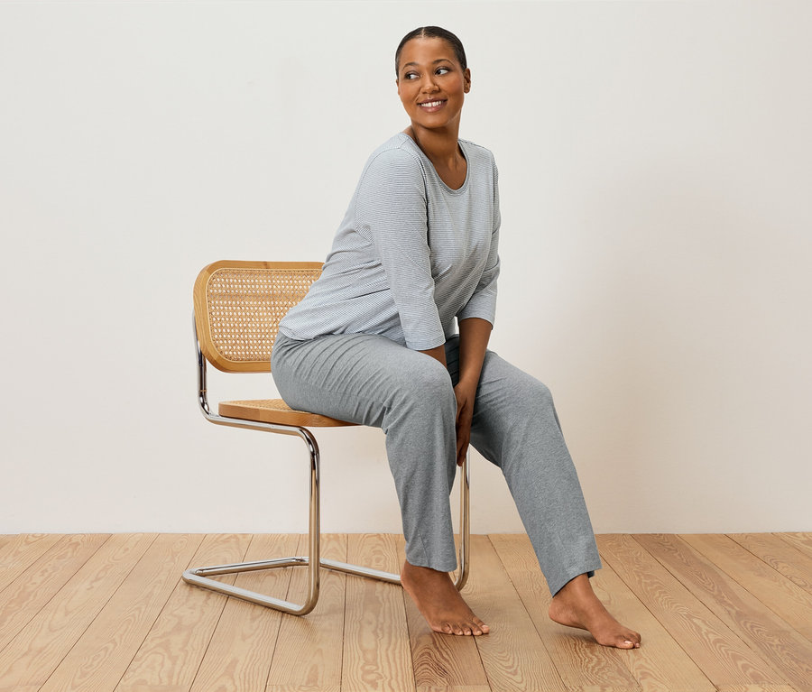 Frau sitzt auf einem Stuhl und trägt einen grau-weiß gestreiften Pyjama.