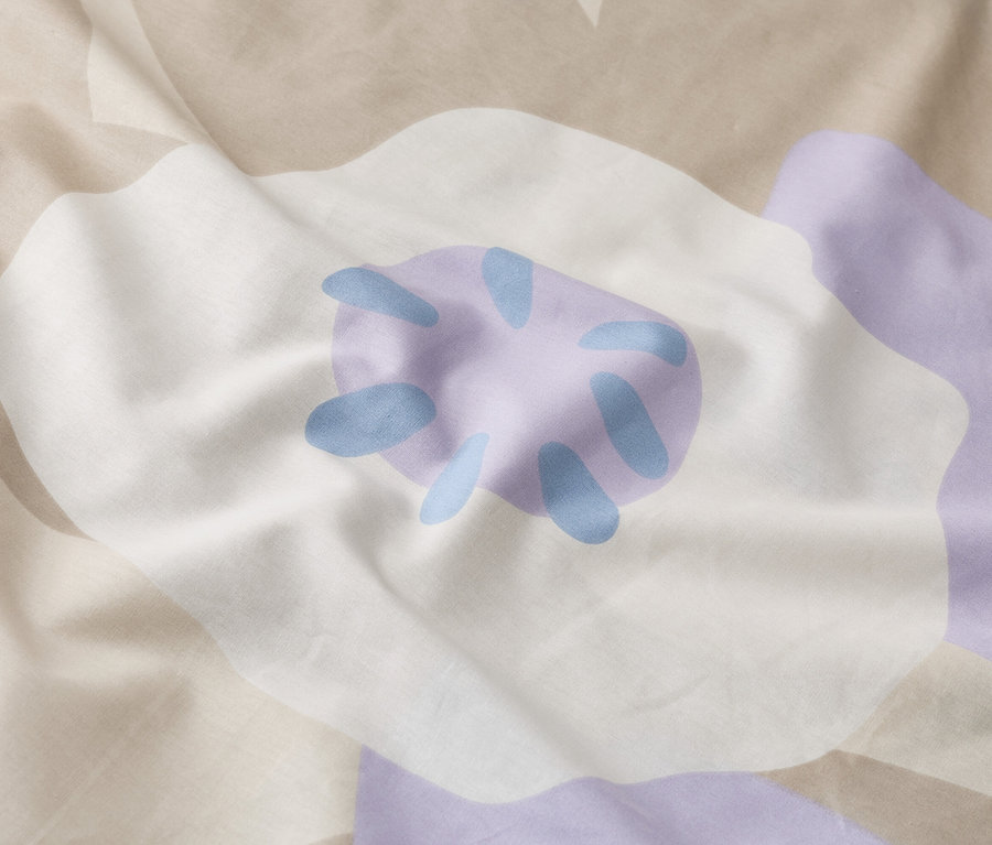 Nahaufnahme von zerknitterter Bettwäsche mit großem floralem Muster in Weiß, Lila und Beige.