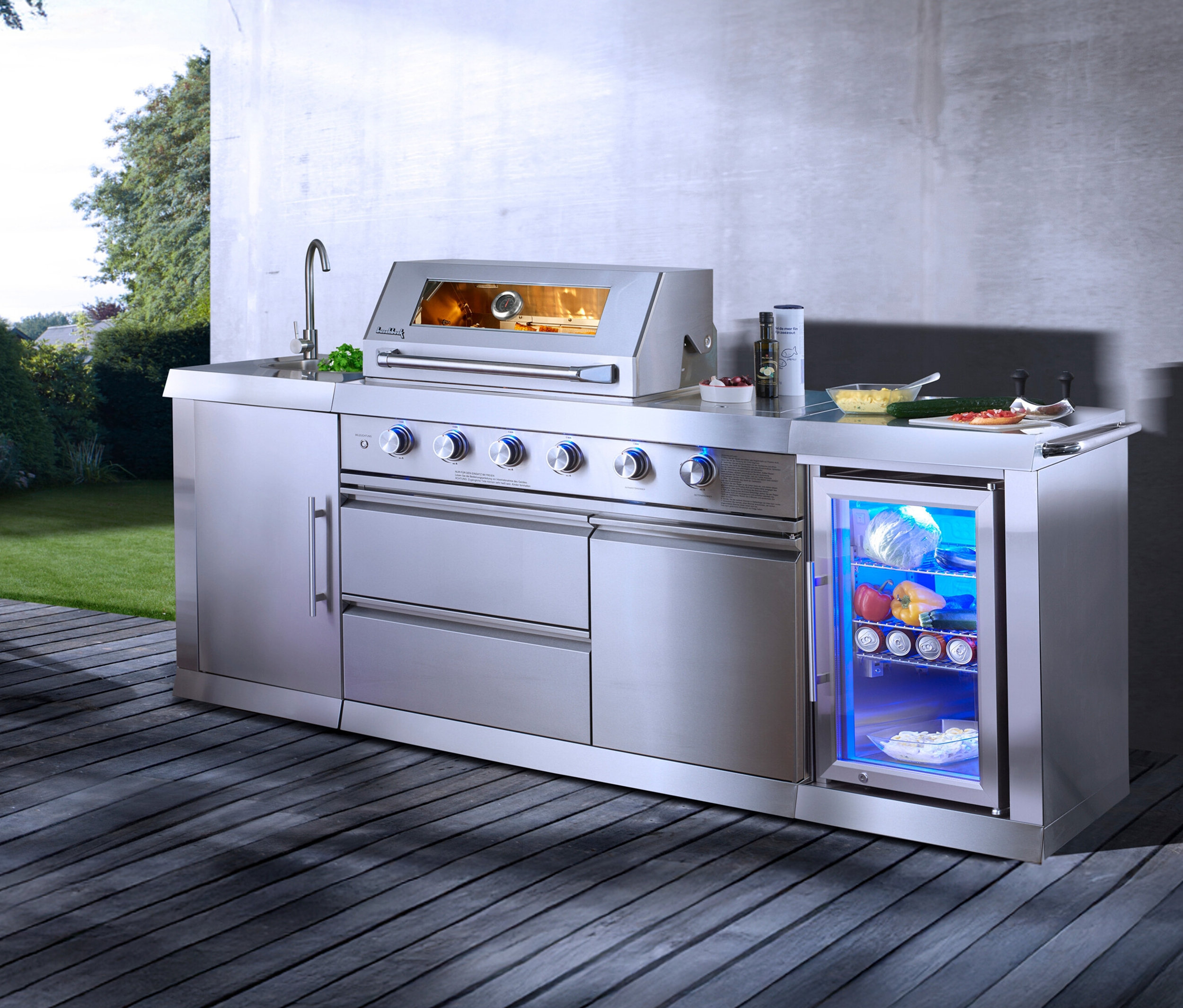 Die Buschbeck Outdoorküche »Oxford« inklusive Wetterschutzhaube steht auf einer Holzterrasse.