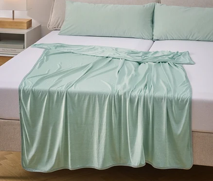 Ein mintgrünes Spannbetttuch und zwei Kissen liegen auf einem Bett mit weißer Bettwäsche.
