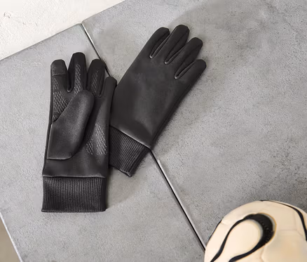 Paar schwarze Handschuhe und ein Fußball liegen auf einer grauen Oberfläche.