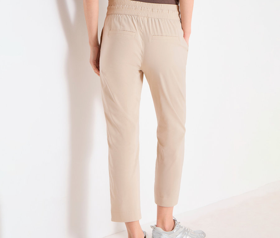 Person von hinten in CECIL Joggpants »Tracey« in Beige und silbernen Turnschuhen vor einer weißen Wand.