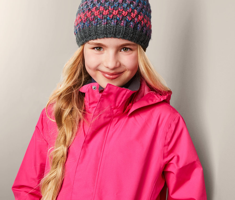 Lächelndes Mädchen trägt eine Strickmütze und eine pinke Jacke.