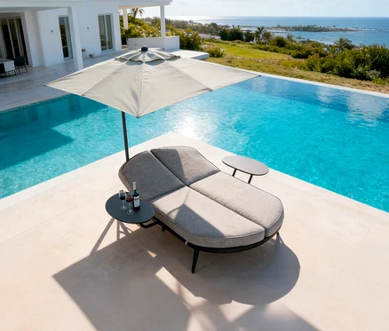 Ein grauer Liegestuhl mit Sonnenschirm steht neben einem Pool. Zwei Weingläser und eine Flasche Wein stehen auf einem Tisch.