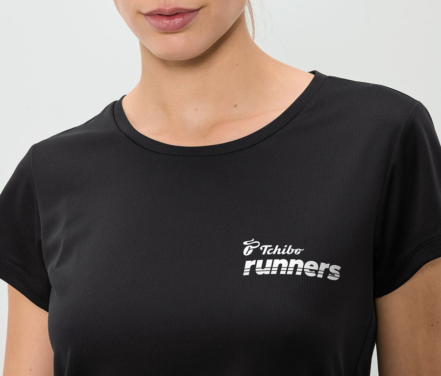 Nahaufnahme einer Frau, die ein schwarzes T-Shirt mit dem Aufdruck "Tchibo runners" trägt.