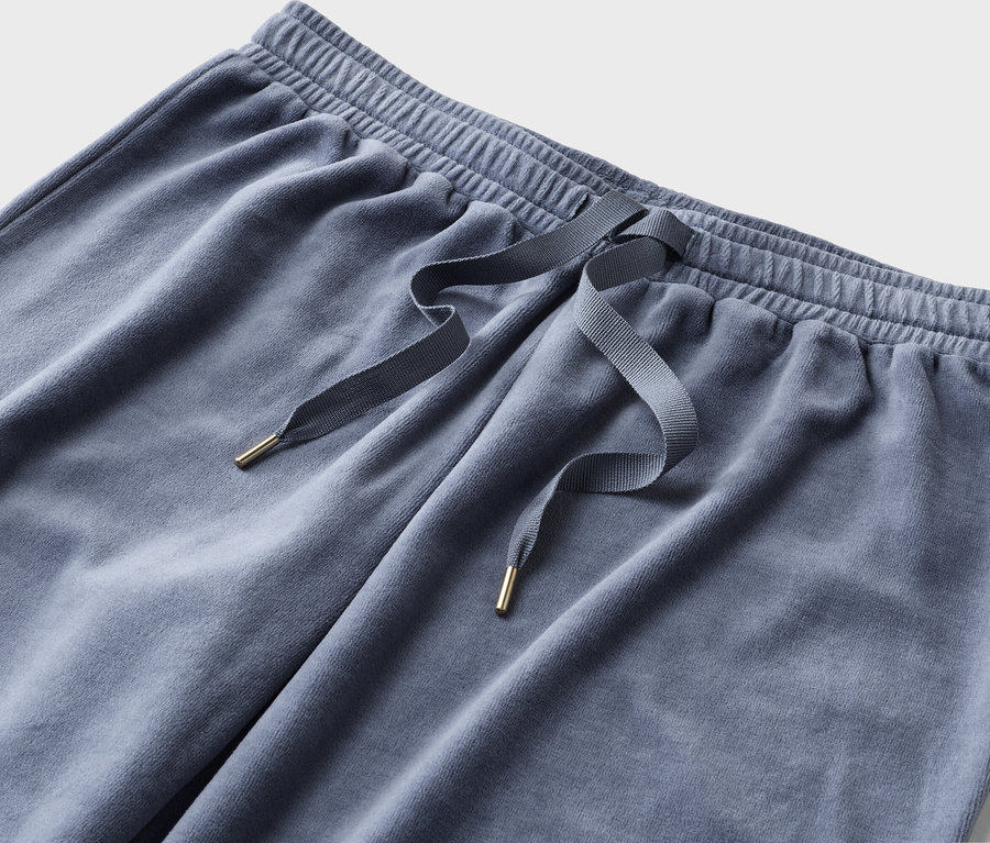 Nahaufnahme einer blaugrauen Jogginghose mit Kordelzug und goldenen Details vor einem weißen Hintergrund.
