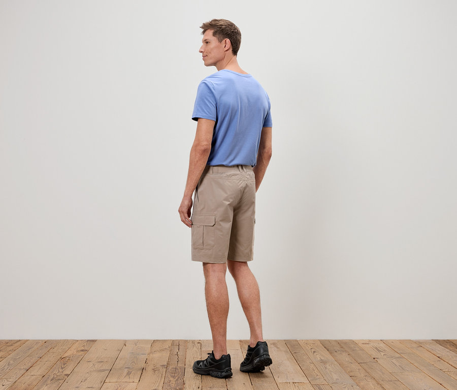 Ein Mann steht mit dem Rücken zur Kamera, er trägt ein blaues T-Shirt, beige Cargo-Shorts und schwarze Turnschuhe.