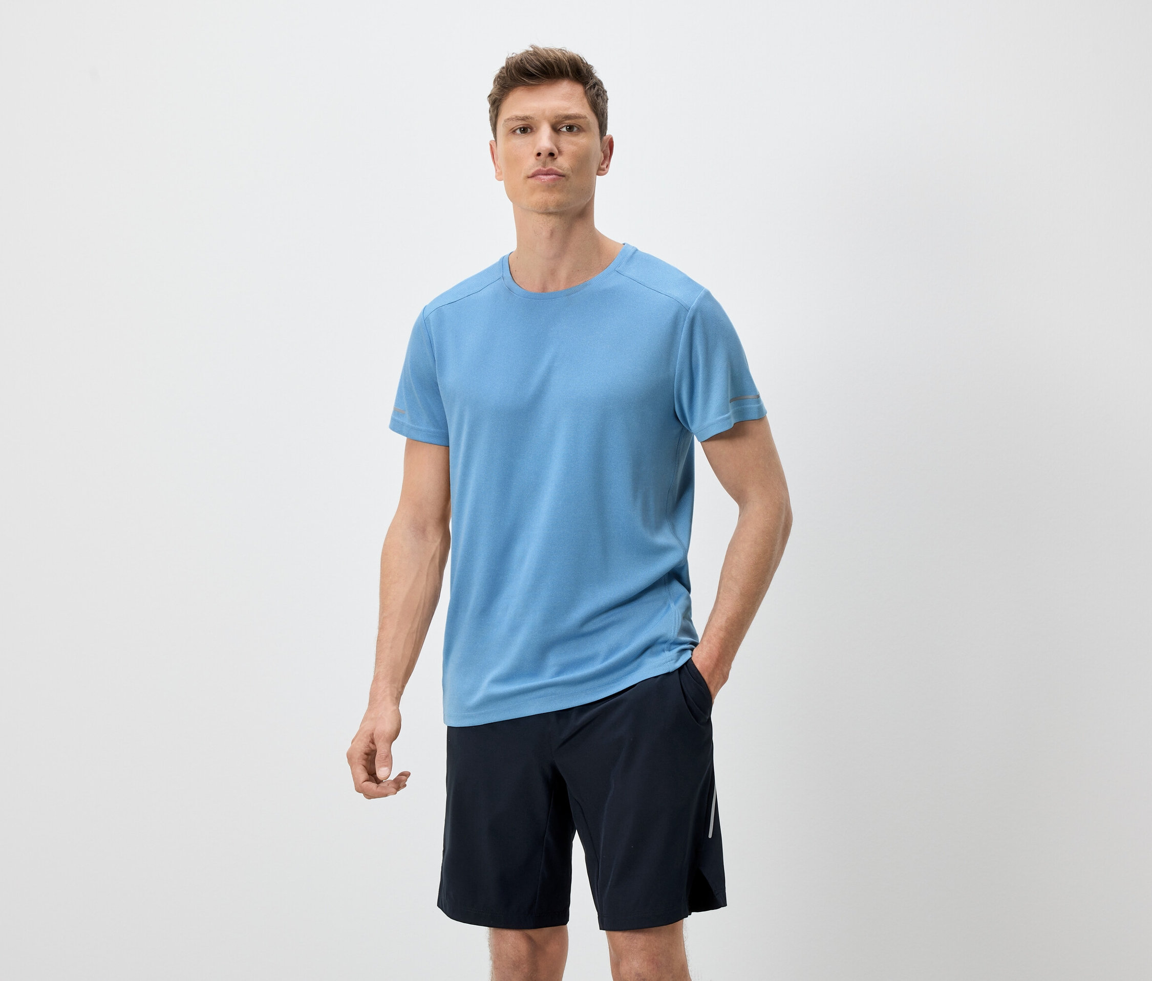 Mann mit blauem T-Shirt und schwarzen Shorts vor einem weißen Hintergrund.