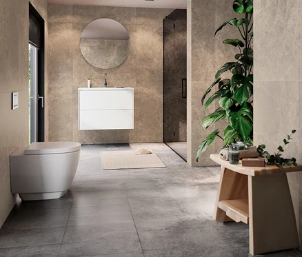 Modernes Badezimmer mit beigefarbenen Fliesen. Links eine wandhängende Toilette. In der Mitte ein weißer Waschtisch »Bodera« inkl Becken, 81 cm breit, mit rundem Spiegel darüber. Rechts eine Glasdusche, eine große Pflanze und ein Holzhocker mit Handtüchern.