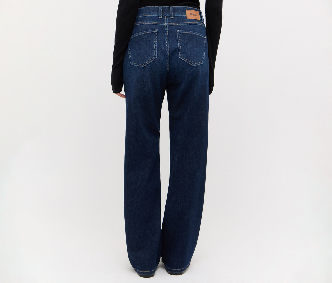 Person von hinten, trägt dunkelblaue Jeans mit weitem Bein und ein schwarzes Langarmshirt. Die Jeans hat sichtbare Gesäßtaschen und einen hellbraunen Aufnäher am Bund.