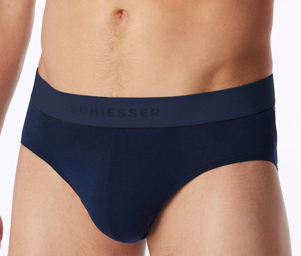 Nahaufnahme eines Männer-Oberkörpers, der dunkelblaue Slips mit „SCHIESSER“ am Bund trägt.