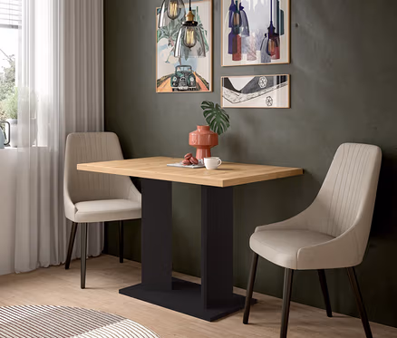 Ein Essbereich mit einem Holztisch und zwei beigen Stühlen. Auf dem Tisch stehen eine rosa Vase, eine Tasse und Macarons. An der dunkelgrauen Wand hängen drei Bilder und zwei Pendelleuchten.