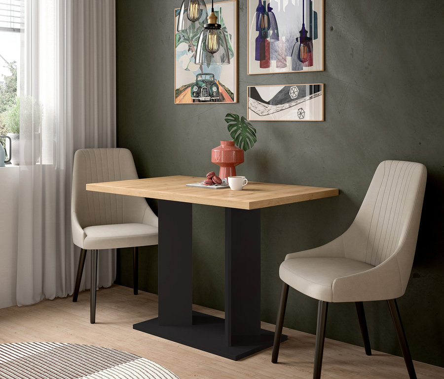 Ein Essbereich mit einem Holztisch und zwei beigen Stühlen. Auf dem Tisch stehen eine rosa Vase, eine Tasse und Macarons. An der dunkelgrauen Wand hängen drei Bilder und zwei Pendelleuchten.