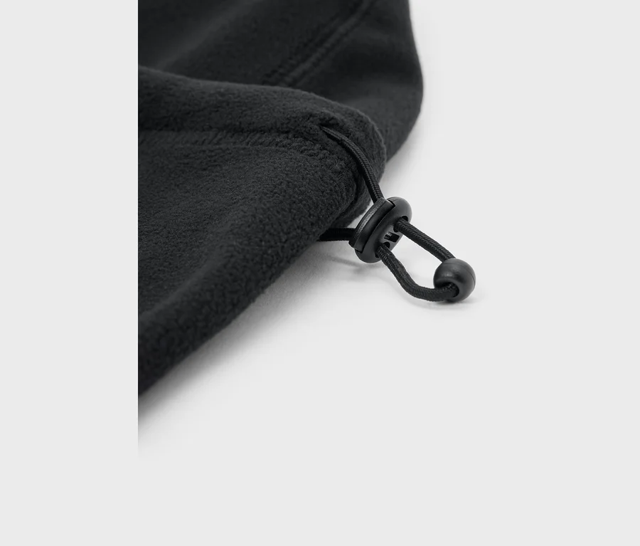 Nahaufnahme von schwarzem Fleece-Stoff mit einem schwarzen Kordelzug und Kordelstopper vor weißem Hintergrund.