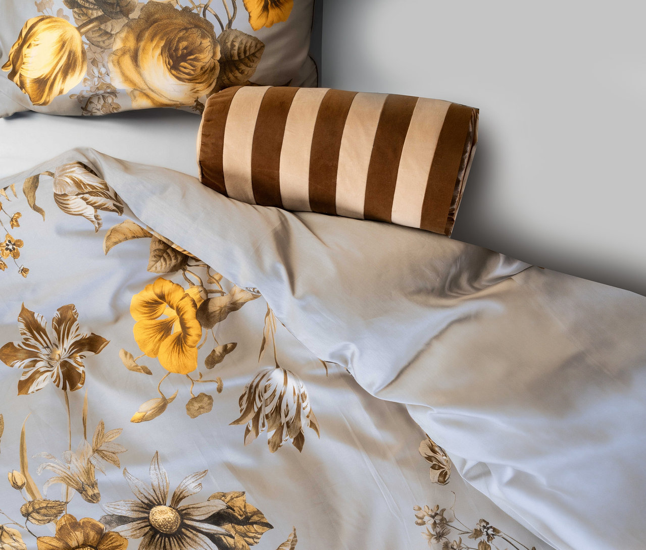 Bett mit floraler Bettwäsche in Gelb- und Brauntönen. Darauf liegt ein braun-beigefarben gestreiftes Essenza Samt-Dekokissen »Bell«.