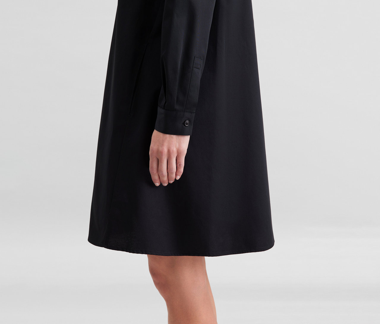 Person trägt ein schwarzes langärmeliges Kleid mit geknöpften Manschetten, wobei Hand und Oberschenkel sichtbar sind.