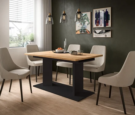 Ein modernes Esszimmer mit hellem Holztisch, schwarzem Untergestell und vier beigen Polsterstühlen. Drei Pendelleuchten hängen über dem Tisch, auf dem eine Schale Orangen und Kerzen stehen. Links ist ein Fenster, an der dunklen Wand hängt abstrakte Kunst.