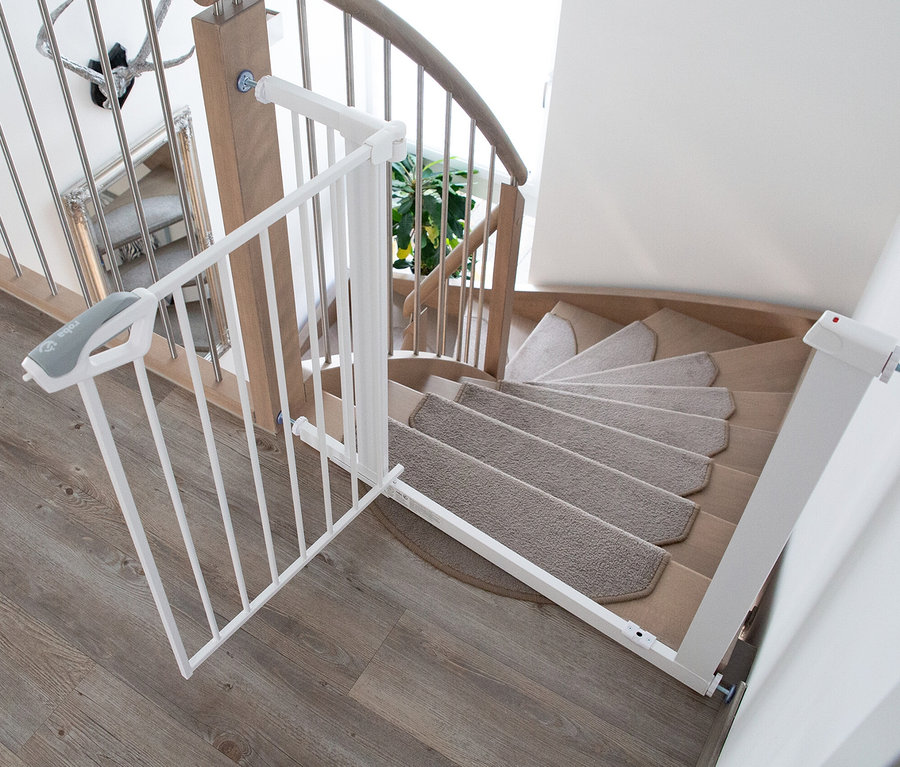 Weißes roba easySafe+ Tür-und-Treppen-Schutzgitter, geöffnet am oberen Ende einer Holzwendeltreppe mit Teppichstufen.